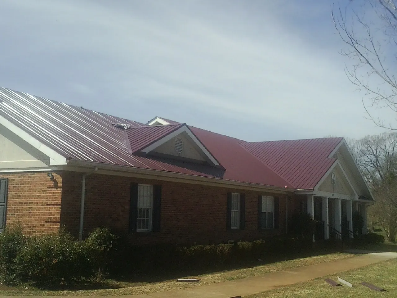 Red metal roof with gabled entries on a long brick building, from a Hail Damage Roof Repair job in Selma