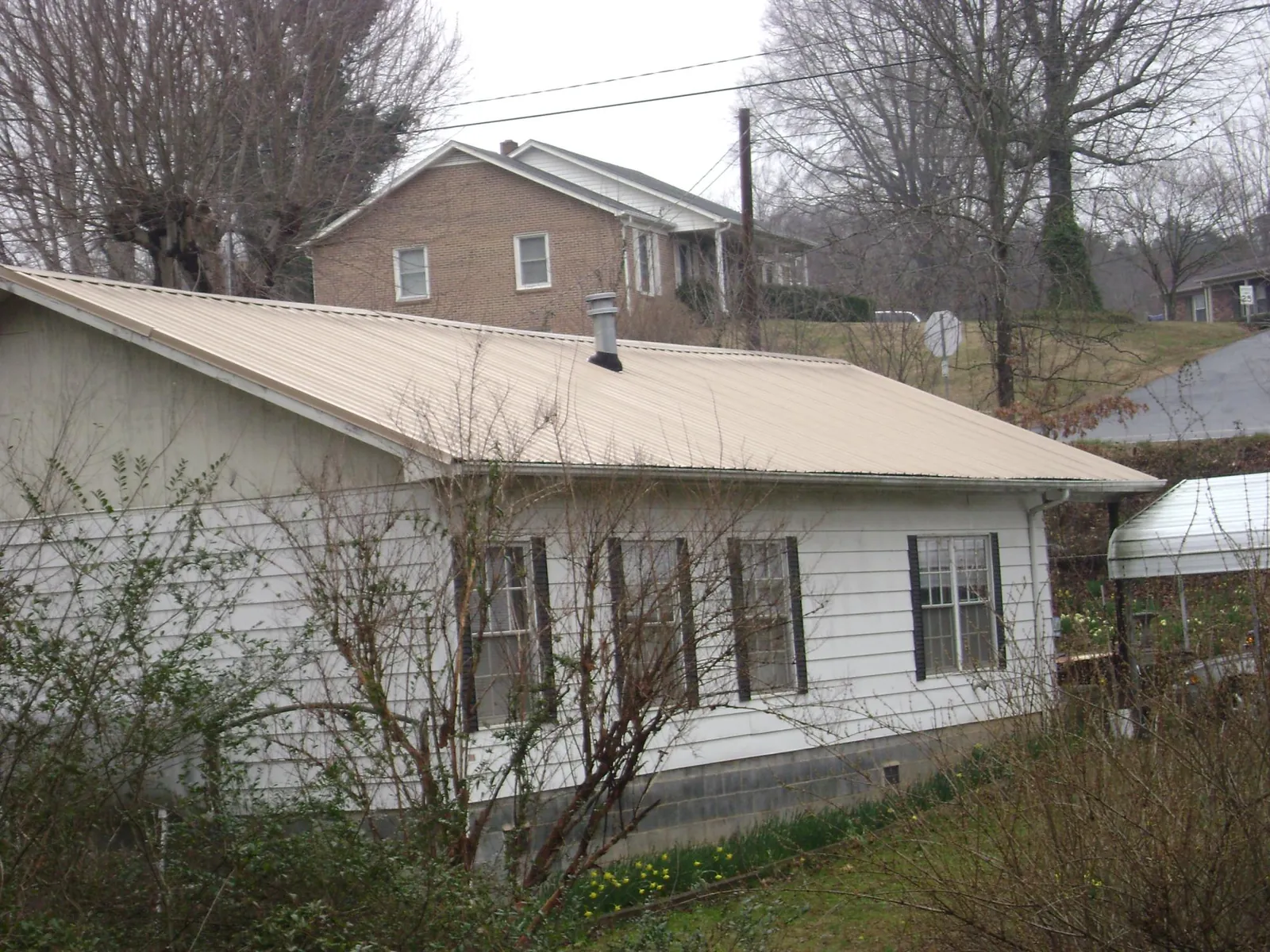 Tan metal roof on a white sided house set into a hillside — Commercial Roofing by Roofing Brothers in Selma